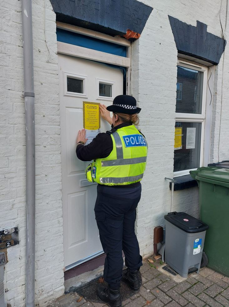Uniformed police officer attaching closure order paperwork to a front door