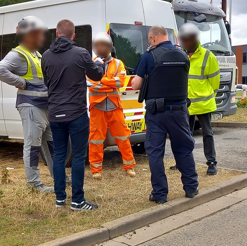 Two police officers with their backs to the camera talking to three construction workers