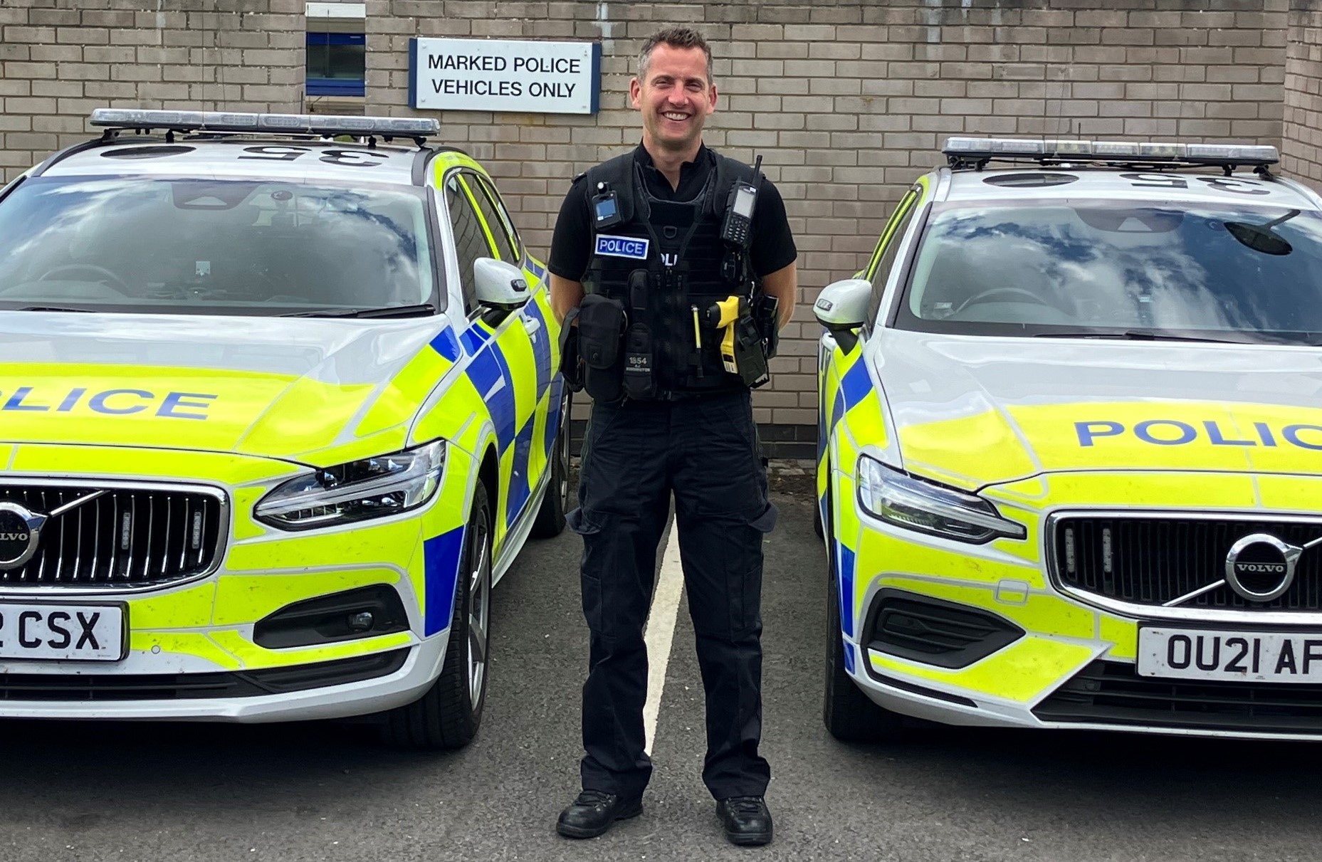 A police officer standing infront of police cars. 