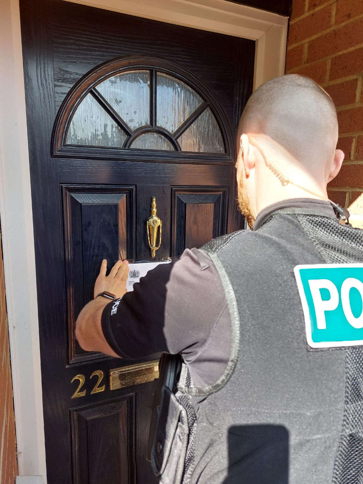 A police officer attaching a copy of the order to the front door