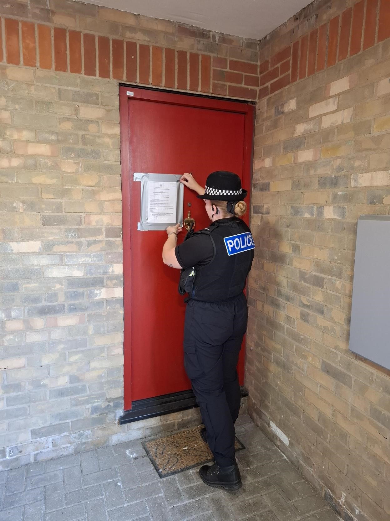 A police officer in uniform taping the closure order to a red door.